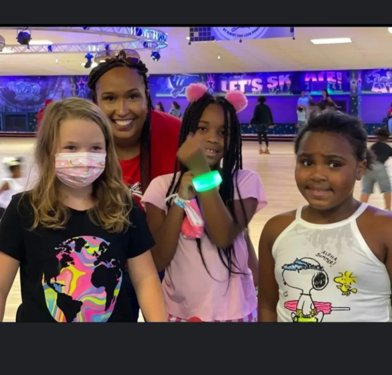 Four people smiling at a roller rink, with neon lights and skate rentals