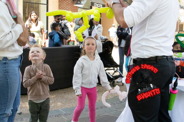 Children watch a street performer with bright yellow balloon animals