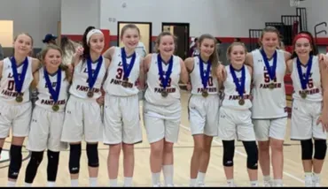 Youth basketball team in white jerseys wearing medals posed together indoors.