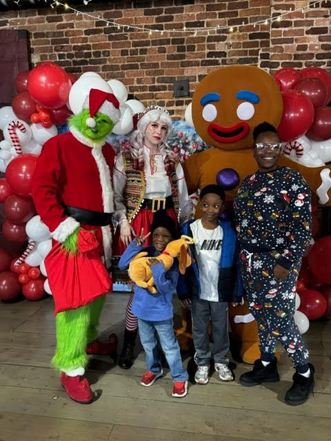 Costumed characters posing with children in front of a brick wall and red balloon backdrop